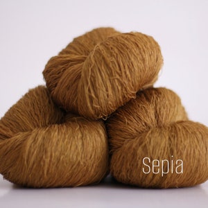 May include: Three skeins of brown yarn, stacked on top of each other. The yarn is a soft, fuzzy texture. The word "Sepia" is printed on the bottom skein.