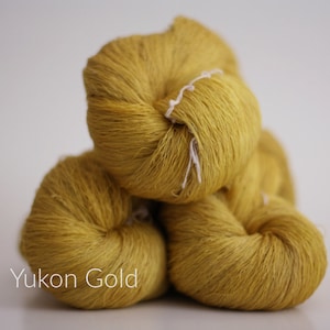 May include: Three skeins of yarn in a golden yellow color, stacked on top of each other. The yarn is labeled "Yukon Gold".