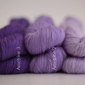 May include: Three skeins of yarn in shades of purple, from darkest to lightest. The skeins are labeled "Amettrine 3", "Amettrine 2", and "Amettrine 1".