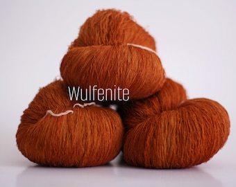 May include: Three skeins of orange yarn, stacked on top of each other. The yarn is labeled "Wulfenite".