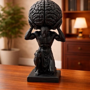 Pode incluir: Escultura preta de uma figura ajoelhada sustentando um grande cérebro. A figura é musculosa e detalhada, com um tecido drapeado ao redor da cintura. A escultura está sobre uma base retangular, colocada em uma superfície de madeira.