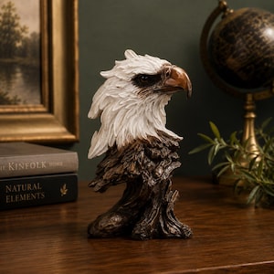 May include: A detailed sculpture of an eagle's head, featuring a white feathered head and a brown beak. The sculpture is mounted on a textured, brown base, and is set against a backdrop of a globe and framed artwork.