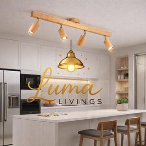 May include: A modern kitchen with white cabinets and a white countertop. A wooden track light with four adjustable spotlights is mounted on the ceiling. A gold-colored pendant light hangs below. The text "Luma LIVINGS" is displayed in gold script.
