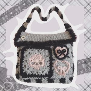May include: A handmade crochet shoulder bag in shades of gray, black, and pale pink. The bag features a skull motif, two heart-shaped appliques with bows, a black fuzzy trim along the top edge, and a striped shoulder strap with star-shaped buttons.