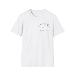 May include: A white short-sleeved t-shirt featuring a small graphic on the upper left chest. The design includes the text "TEAM BRAUT" in an arched font, the name "Lena" in script, a small heart icon, and the text "MALLORCA 2026" below it.