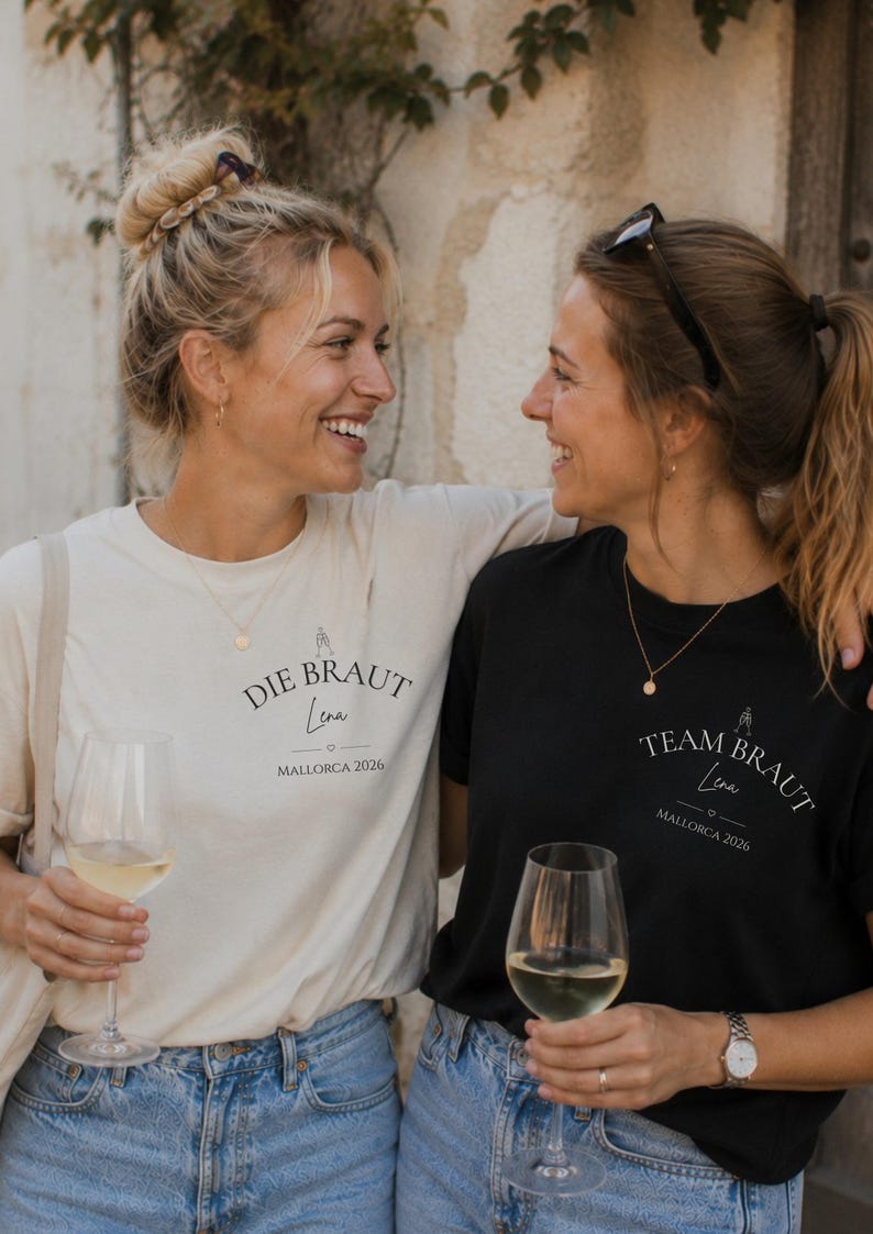 May include: A cream-colored t-shirt with the black text DIE BRAUT Lena MALLORCA 2026 and a black t-shirt with the white text TEAM BRAUT Lena MALLORCA 2026, both featuring a small graphic of a bride and a heart icon on the chest area.