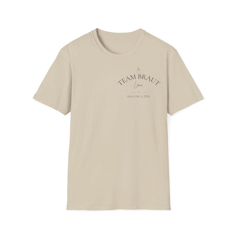 May include: A beige short-sleeve t-shirt featuring dark text on the upper left chest. The text reads TEAM BRAUT, followed by the name Lena in script, a small heart icon, and the text MALLORCA 2026. The shirt has a crew neckline and a plain back.