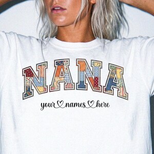 May include: White t-shirt featuring the word "NANA" in a patchwork design. Underneath, the phrase "your names here" is written in cursive, with heart symbols. The shirt has a crew neck.