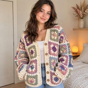 May include: A long-sleeve cardigan made of crocheted granny squares in muted shades of cream, sage green, dusty rose, and periwinkle blue. The garment features a V-neckline, a cream-coloured ribbed trim, and five round brown buttons down the front.