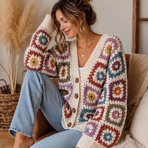 Könnte beinhalten: Eine langärmelige Strickjacke mit V-Ausschnitt und einem mehrfarbigen Granny-Square-Häkelmuster in Blau-, Gelb-, Lila- und Rosttönen, abgerundet mit einem cremefarbenen Rippstricksaum und vier großen braunen Knöpfen an der Vorderseite.