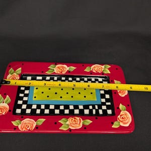 May include: A rectangular ceramic tray with a red border featuring painted orange roses and black dots. The centre has a black and white checkerboard pattern, a blue border, and a lime green rectangle with black dots. A yellow tape measure shows 28 cm.