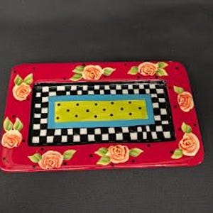 May include: A rectangular ceramic tray featuring a vibrant red border decorated with painted peach-coloured roses and green leaves. The centre displays a black and white checkered pattern surrounding a bright blue frame and a lime green dotted rectangle.