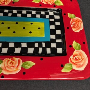 May include: A rectangular ceramic serving tray featuring a vibrant red border decorated with hand-painted peach roses and black polka dots. The centre displays a black and white checkered pattern surrounding a bright lime green rectangle with black dots.