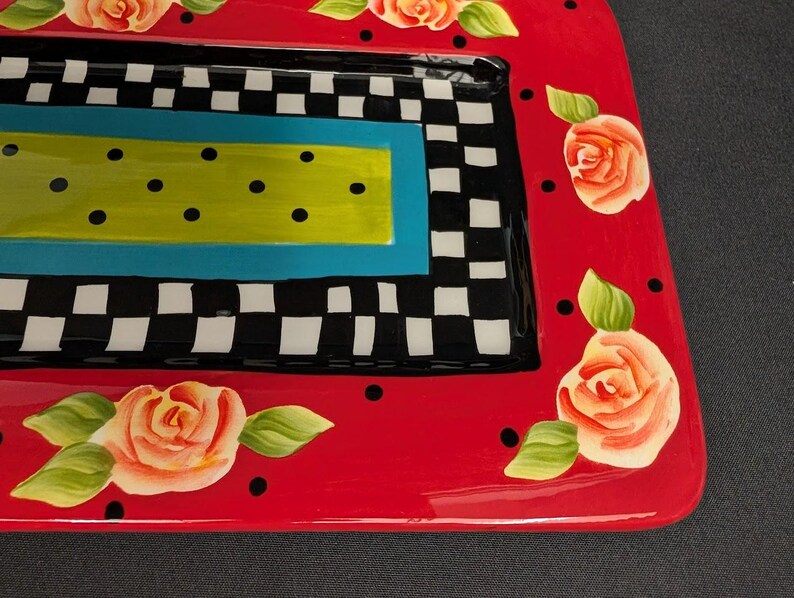 May include: A rectangular ceramic serving tray featuring a vibrant red border decorated with hand-painted peach roses and black polka dots. The centre displays a black and white checkered pattern surrounding a bright lime green rectangle with black dots.