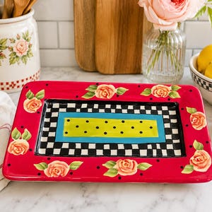 May include: A rectangular ceramic serving tray featuring a vibrant red border decorated with painted peach roses and black polka dots. The centre displays a black and white checkered pattern surrounding a bright blue frame and a lime green rectangle.