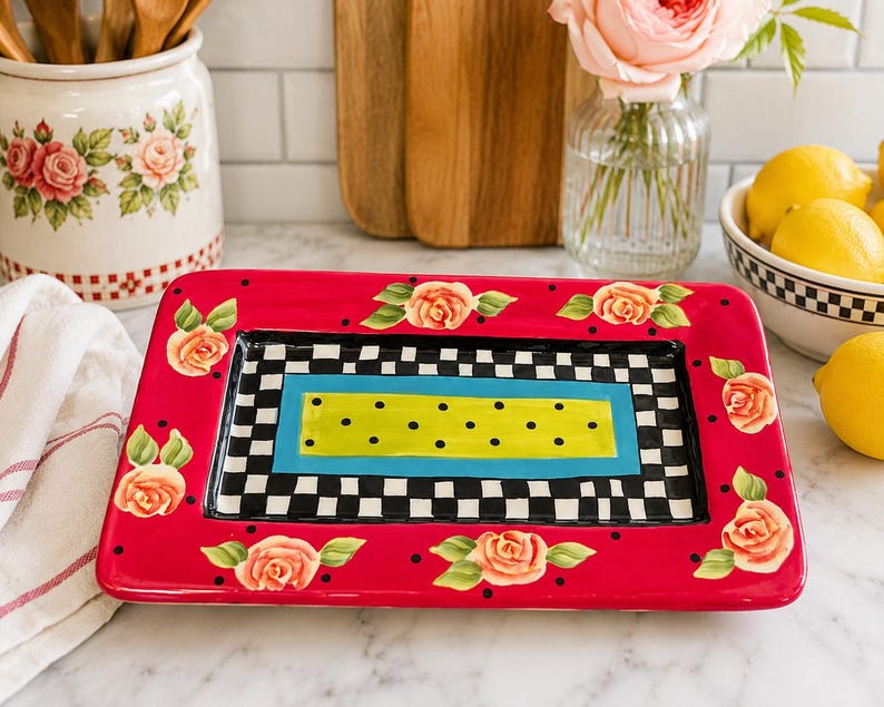 May include: A rectangular ceramic serving tray featuring a vibrant red border decorated with painted peach roses and black polka dots. The centre displays a black and white checkered pattern surrounding a bright blue frame and a lime green rectangle.