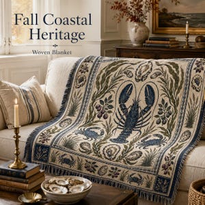 May include: A woven blanket featuring a central dark blue lobster surrounded by crabs, oysters, and botanical elements in shades of green and blue on a cream background. The text Fall Coastal Heritage Woven Blanket is visible.