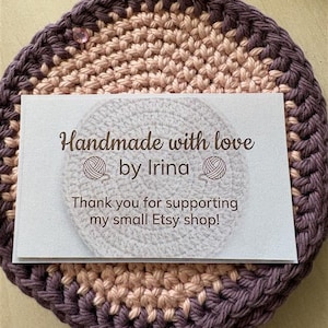 May include: A handmade crochet coaster in shades of purple, tan, and cream. A business card rests on top, with the text "Handmade with love by Irina" and "Thank you for supporting my small Etsy shop!"