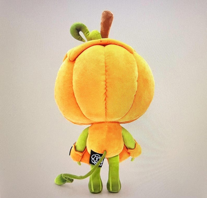 Pode incluir: Uma boneca de ab&oacute;bora de pel&uacute;cia com uma grande cabe&ccedil;a laranja, bra&ccedil;os e pernas verdes e uma longa cauda verde. A boneca tem um caule marrom e uma folha verde encaracolada no topo. Decora&ccedil;&atilde;o de Halloween.