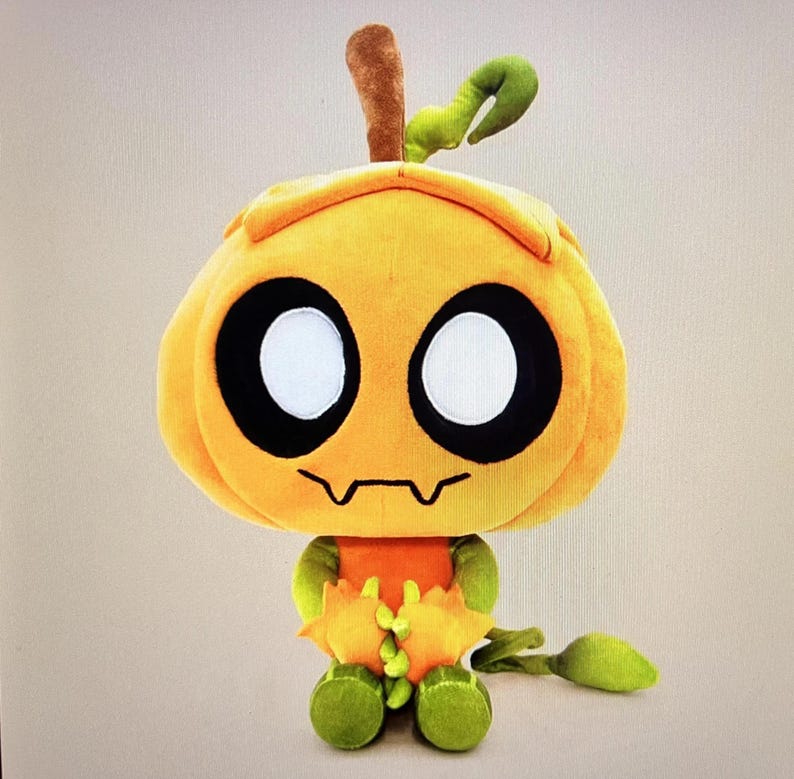 Pode incluir: Um brinquedo de pel&uacute;cia em forma de personagem semelhante a uma ab&oacute;bora. O brinquedo &eacute; principalmente laranja com olhos grandes pretos e brancos, uma boca irregular e detalhes verdes e marrons. Possui um caule e detalhe de folha no topo e p&eacute;s verdes.