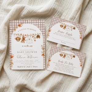 May include: A baby shower invitation set featuring a brown and white gingham pattern with autumn leaf accents. The cards display illustrations of a teddy bear, baby clothes, and shoes on a clothesline, with text including A Little Pumpkin is on the way.