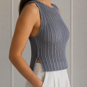 May include: A sleeveless, slate blue knit top with a ribbed texture. The top has a round neckline and a side slit. The model is wearing the top with white pants. The top is a stylish addition to any wardrobe.