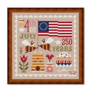 Op de afbeelding: Kruissteekontwerp in een houten frame. Toont een koloniale Amerikaanse vlag, bijen, een bijenkorf, een taart en de tekst "4th of July 250 Years". Het ontwerp bevat een pot honing, een hart en een bloem. De woorden "White Duck Stitching" zijn ook opgenomen.