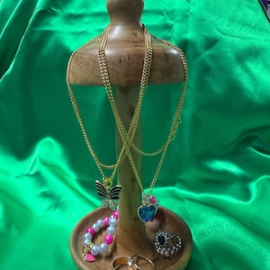May include: A wooden jewelry display stand holding gold chain necklaces with butterfly and heart pendants, a bracelet, and rings. The jewelry is displayed against a green background.