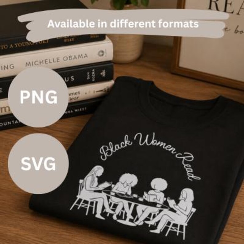 May include: A black t-shirt featuring a white line art graphic of four individuals sitting at a table reading books. The text "Black Women Read" is printed in a white cursive font above the illustration. The shirt is displayed on a wooden surface.