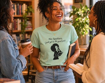 May include: A light mint green t-shirt featuring a black graphic of a person with curly hair reading a book, with the text "No Spoilers, I just got to the good part" printed in black ink above the illustration, paired with blue denim jeans.