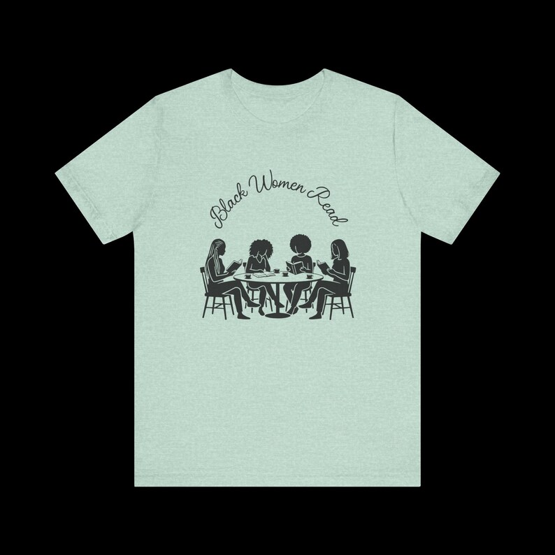 May include: A light green heathered t-shirt featuring a black graphic of four individuals sitting at a round table reading books. Above the illustration, the text Black Women Read is printed in a black cursive font. The shirt has short sleeves.