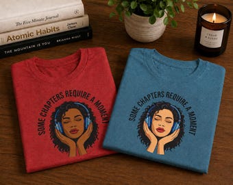 May include: Two crew neck t-shirts, one red and one blue, each featuring a graphic of a person with curly hair wearing blue headphones. The text "SOME CHAPTERS REQUIRE A MOMENT" is printed in a circular arc above the illustration on both shirts.