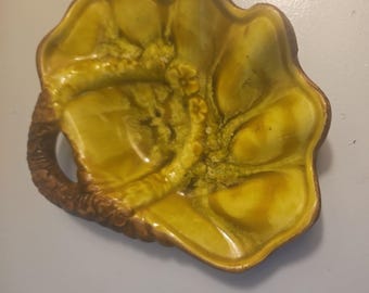 May include: A ceramic bowl with a glossy mustard yellow glaze and a brown textured handle. The bowl features a scalloped, organic shape with raised floral details and a mottled finish, showcasing a deep yellow color palette with brown accents.