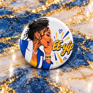 May include: A circular pinback button featuring an illustration of a person with dark braided hair, wearing a blue blazer over a yellow top, a pearl necklace, and beaded bracelets. The text EE-yip is printed in yellow with blue outlines.