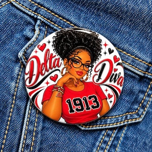 May include: A circular pinback button featuring an illustration of a person with curly hair and glasses wearing a red shirt with the text 1913. The design includes the text Delta Diva, red hearts, and black accents on a white background.