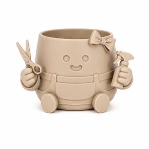 May include: A light beige silicone planter shaped like a character wearing overalls and a bow. The figure has a smiling face and holds a pair of scissors in one hand and a spray bottle in the other. The design is monochromatic with a smooth finish.