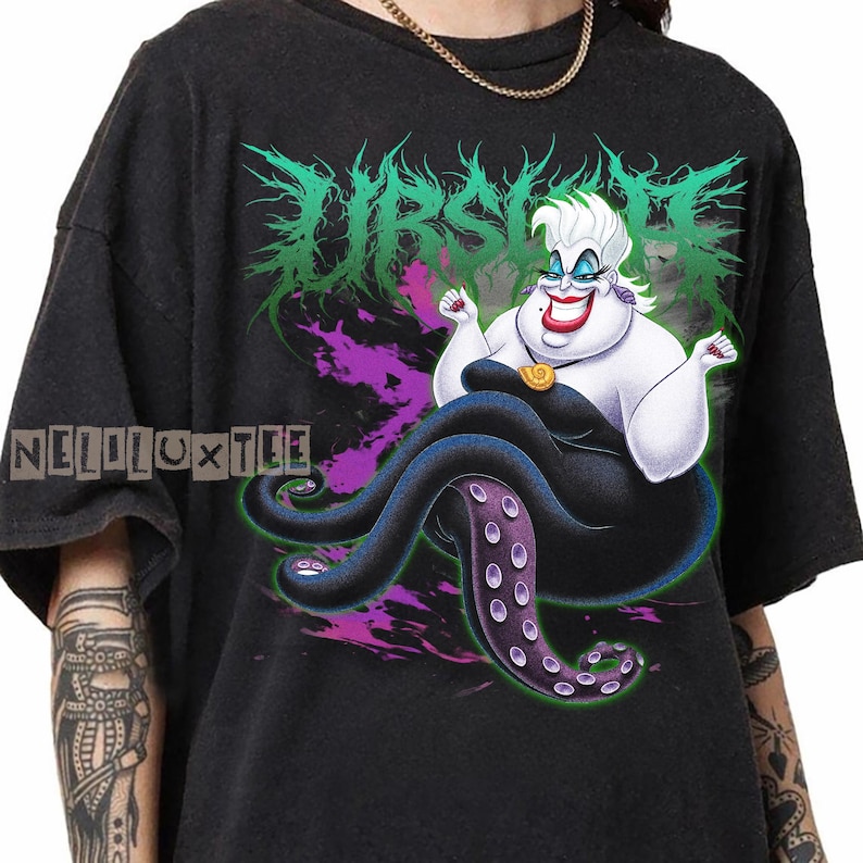May include: Black t-shirt featuring a cartoon illustration of Ursula from The Little Mermaid. The design includes the word "URSULA" in green and purple, with the character's image in the center. The shirt also has the text "NELLOLUXTEE".