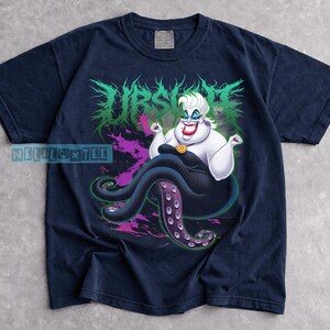 May include: Navy blue t-shirt featuring a graphic of Ursula from The Little Mermaid. The design includes Ursula with her tentacles, the word "Ursula" in green, and purple accents. The shirt is a comfortable, casual wear.