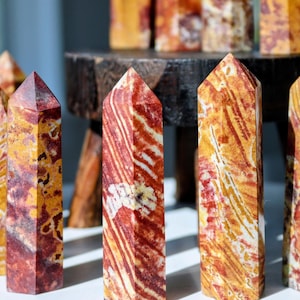 May include: A collection of polished stone towers featuring a natural pattern of swirling red, orange, yellow, and white colors. Each tower has a hexagonal base and a pointed top, displaying unique mineral striations and a smooth, glossy finish.
