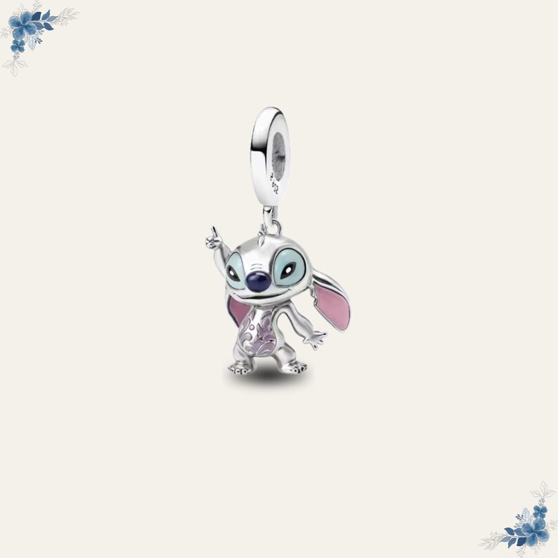 May include: A silver charm featuring the character Stitch from Lilo & Stitch. The charm has blue eyes, pink ears, and purple accents. The charm is suspended from a silver loop.