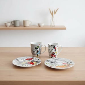 Puede incluir: Un juego de dos tazas de cerámica y dos platos con diseños de Mickey y Minnie Mouse. Las tazas tienen un fondo gris y blanco, mientras que los platos tienen un fondo blanco. Las tazas y los platos están sobre una mesa de madera.