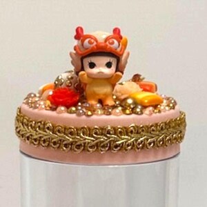 May include: A clear plastic jar with a decorative lid featuring a small figurine. The lid is pink with gold trim and embellishments. The jar contains colorful collectible figures and the text "GOT BEANS!"