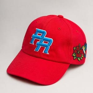 May include: A red baseball cap with the letters "PR" in blue and white embroidery on the front. A floral and hummingbird design is embroidered on the side. The cap is made of a soft, durable fabric.