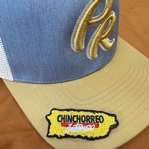 May include: A gray and tan baseball cap with a white mesh back. The cap features a gold embroidered "R" logo and a patch with the words "CHINCHORREO Intenso" in yellow, red, and white, shaped like Puerto Rico.