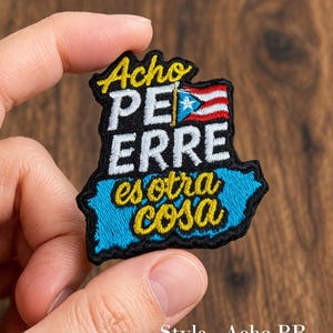 May include: Embroidered patch in the shape of Puerto Rico, featuring the text "Acho Perre Es Otra Cosa" in yellow and white. The patch includes the Puerto Rican flag and a blue outline.