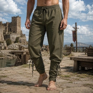 May include: Olive green trousers featuring an elastic waistband with a drawstring closure. The pants have a relaxed fit through the thighs and taper toward the calves, where they are secured with side-lacing details that include matching fabric ties.