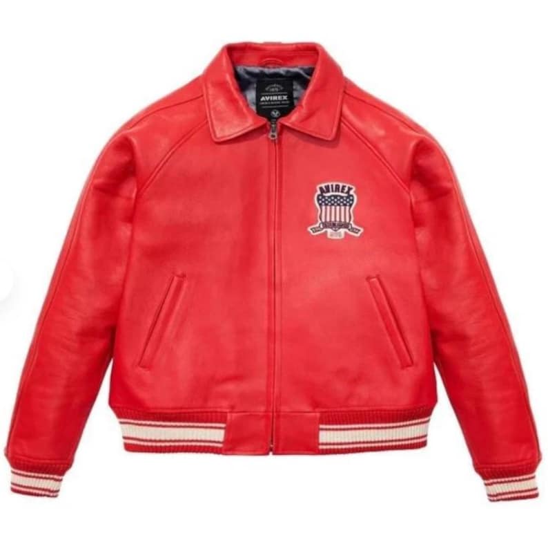 May include: A red leather jacket with a bomber-style design. The jacket features a collar, a zipper closure, and a patch on the chest with the brand name and a patriotic emblem. The cuffs and hem have white and red striped detailing.