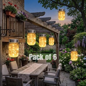May include: A pack of six solar-powered mason jar lanterns featuring silver lids and wire handles, each containing warm yellow string lights. The jars are displayed hanging from a wooden pergola and a metal garden stake in an outdoor setting.