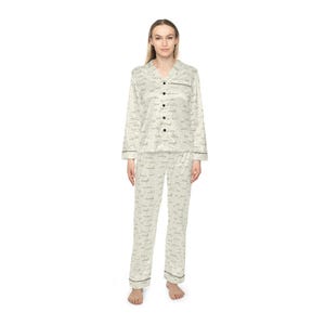 Può includere: Pigiama color crema con camicia abbottonata e pantaloni abbinati. Il set presenta un motivo sottile di piccole parole ripetute in una tonalità più scura, con finiture nere sui polsini, sul colletto e sulle tasche. Il pigiama è realizzato in un materiale morbido e setoso.