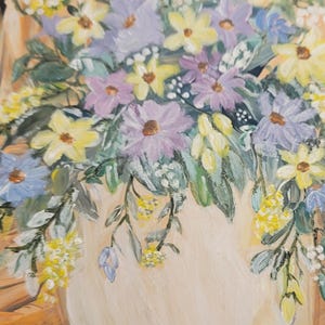 Puede incluir: Pintura al óleo de un jarrón rebosante de flores coloridas. El arreglo presenta flores amarillas, moradas y azules con follaje verde. El jarrón es de color crema suave y el fondo tiene un tono cálido y neutro.
